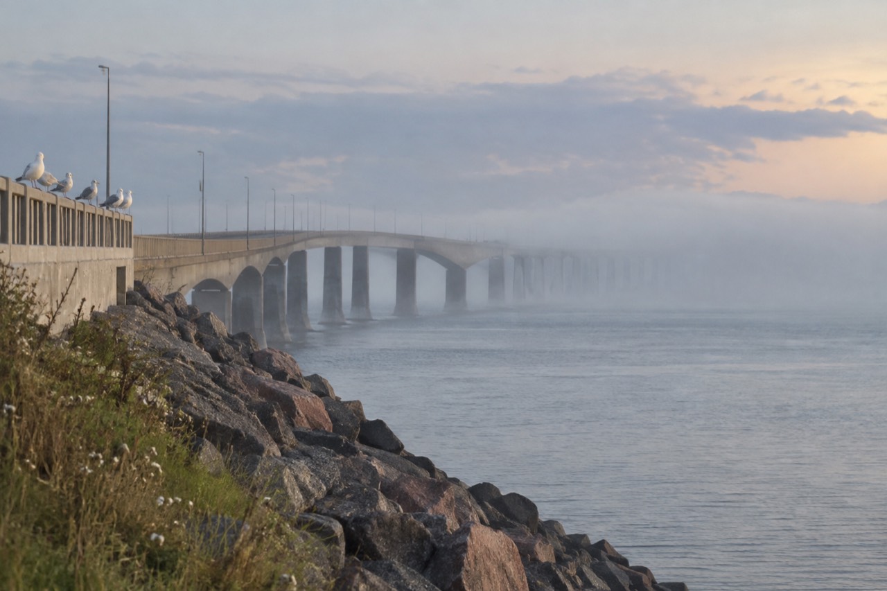 Confederation Bridge curving across the Northumberland Strait toward green Prince Edward Island farmland