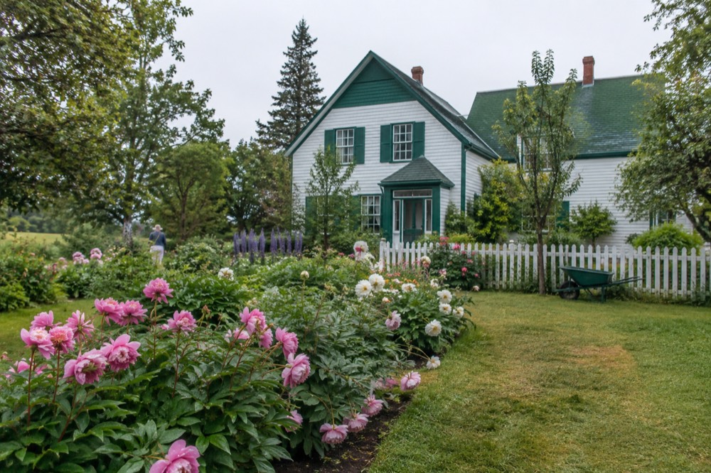 Green gabled farmhouse set among flower gardens under a summer sky