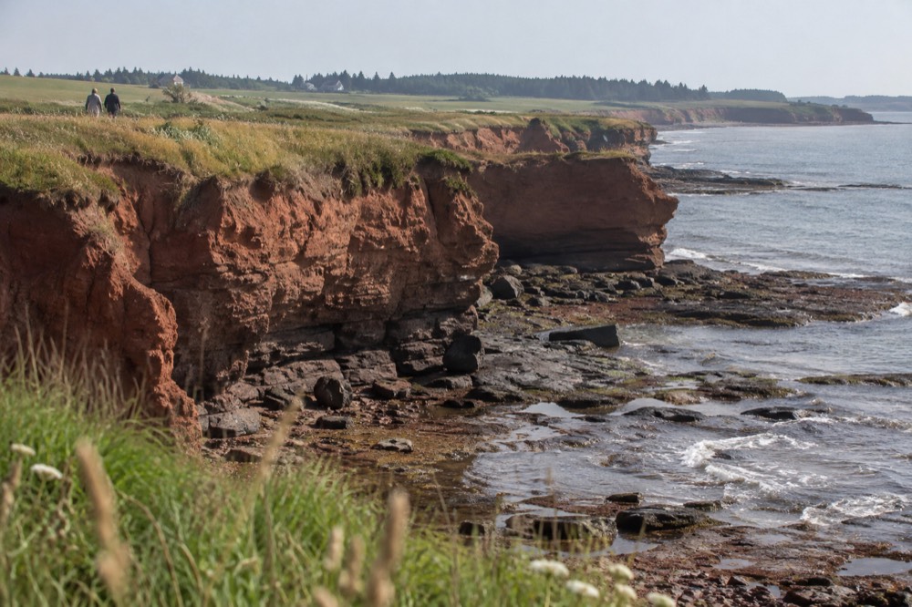 Red sandstone cliffs above a quiet beach with green farmland behind