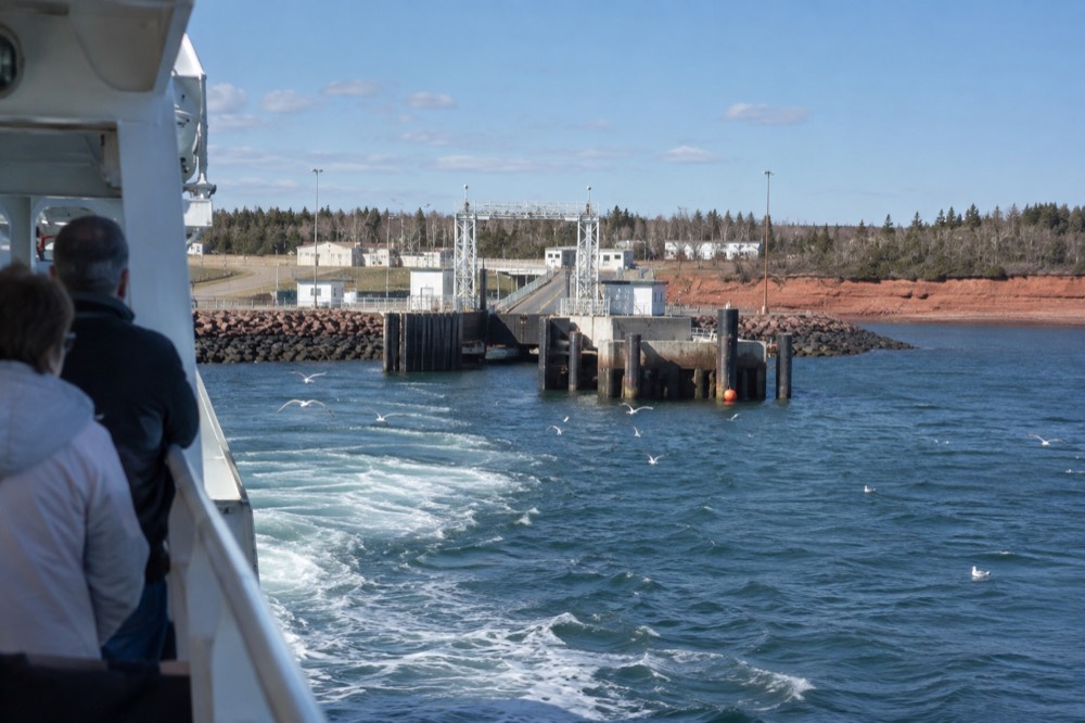 A ferry boat approaching a dock near red cliffs on an island shoreline