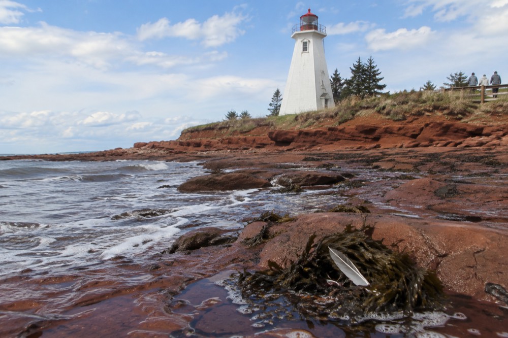 White lighthouse standing above a red rock shoreline