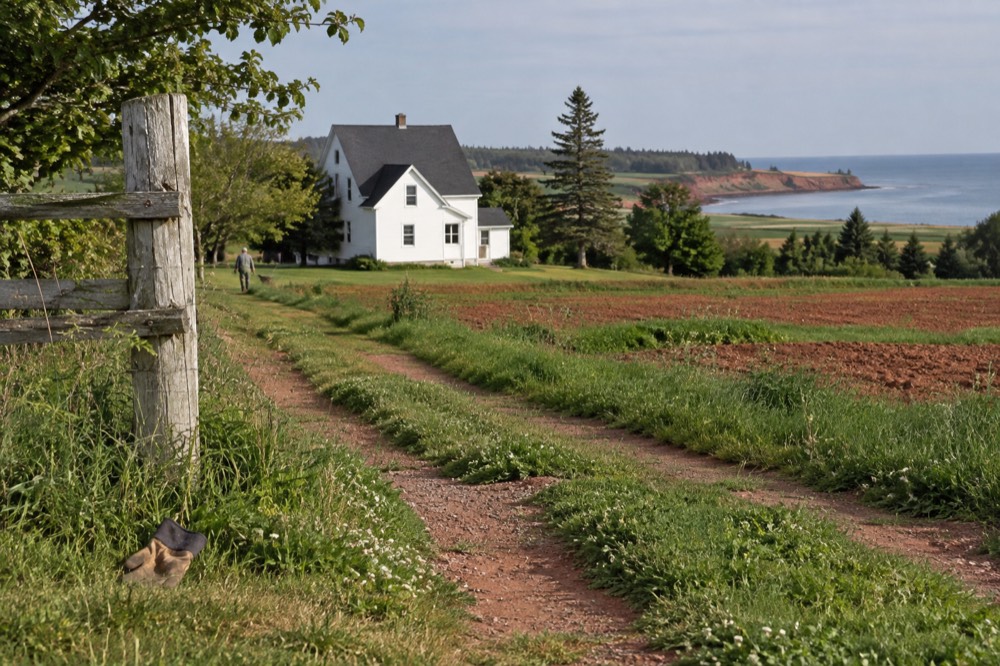 Rolling green farmland with a white farmhouse and red soil fields in the distance