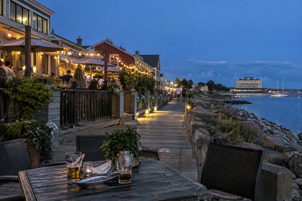 A harbourfront street with patios and string lights at dusk