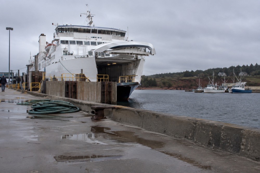 A red and white ferry docked at a small Island wharf with fishing boats nearby