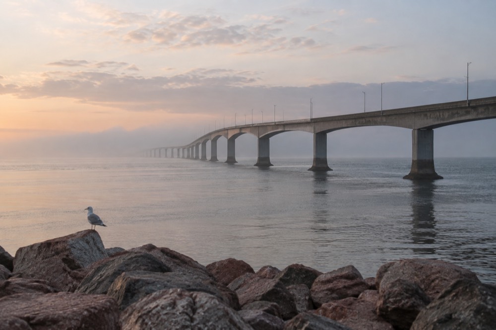 A long fixed bridge stretching over calm sea toward low green coastline