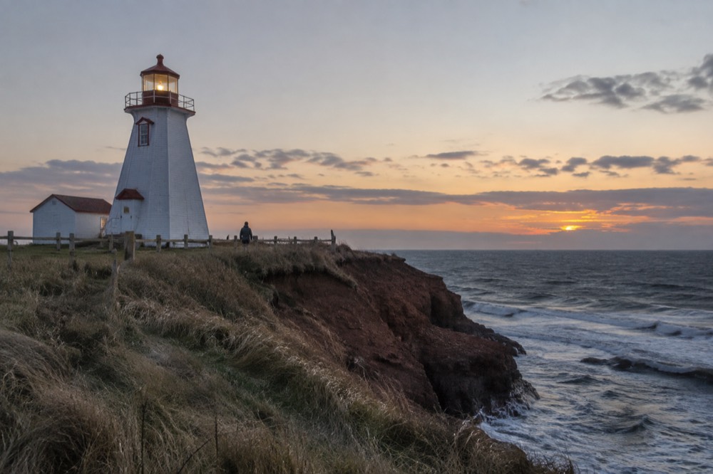 A white lighthouse on a red cliff overlooking open water at dusk