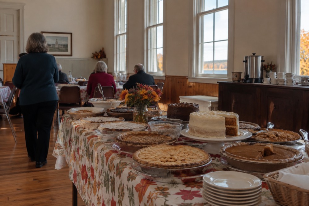 A long harvest table set with pies and cakes inside a community hall