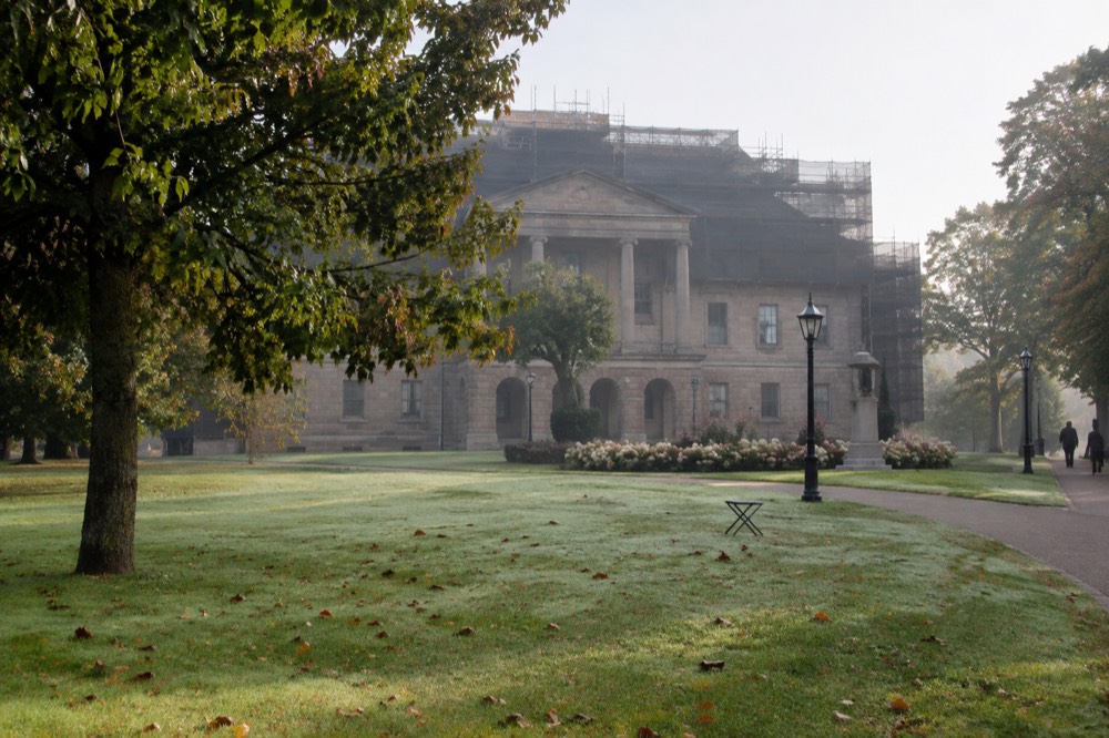 A historic stone government building with columns, viewed from an open green lawn