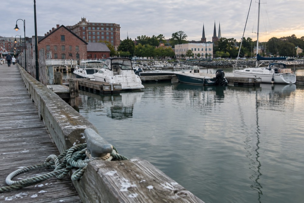 A wooden wharf with small boats moored beside historic brick buildings at the harbour
