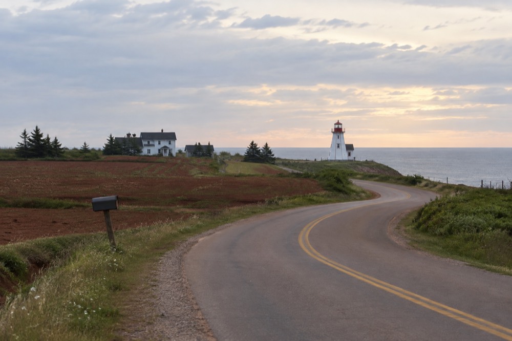 A quiet two-lane road curving through red farmland toward the sea