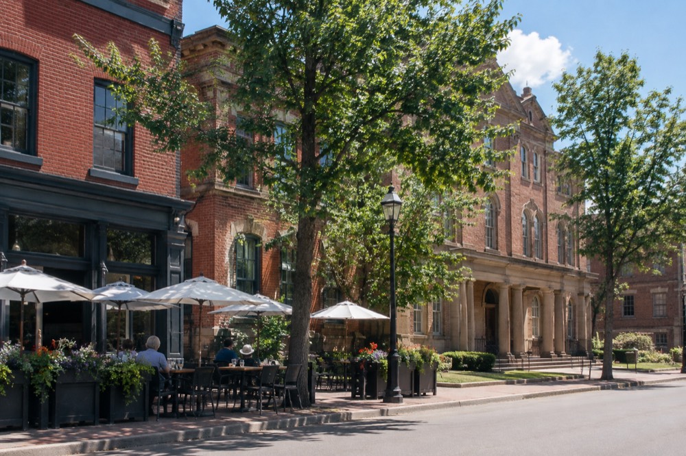 A historic street with brick storefronts and outdoor patios in summer