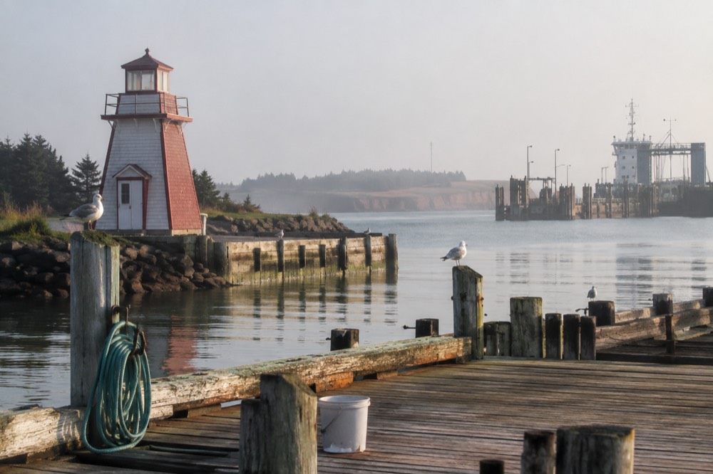 A small red lighthouse and wooden wharf beside calm water in a Prince Edward Island village