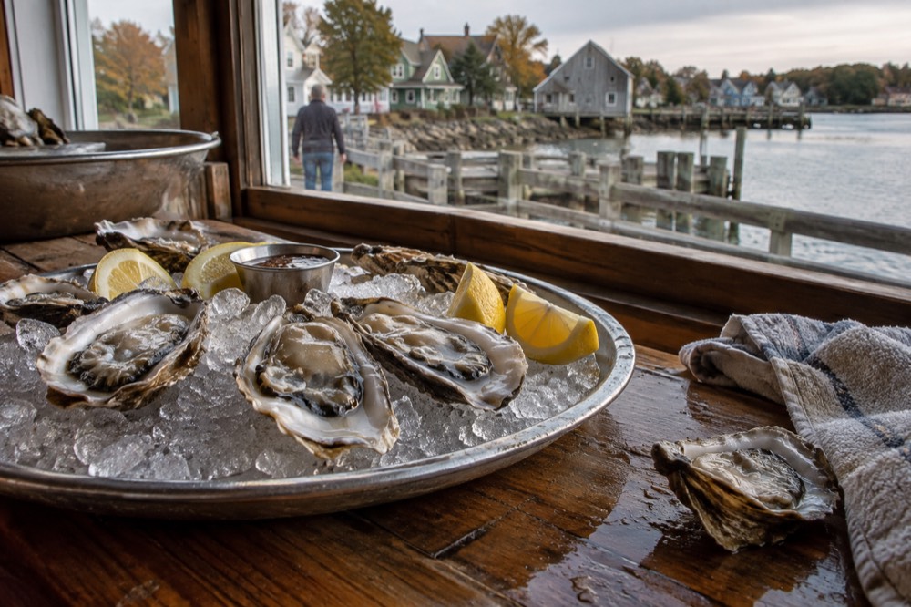 A tray of shucked oysters on ice beside lemon wedges on a wooden counter