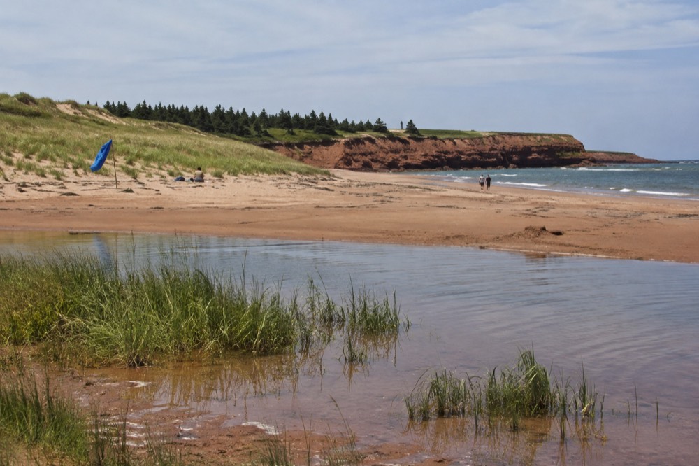 Wide sandy beach with grass-topped dunes and red cliffs on a calm day