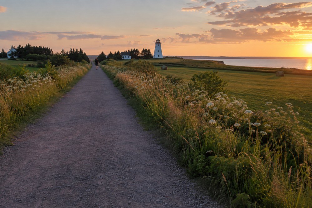 Stone-dust trail cutting through green farmland toward a distant lighthouse