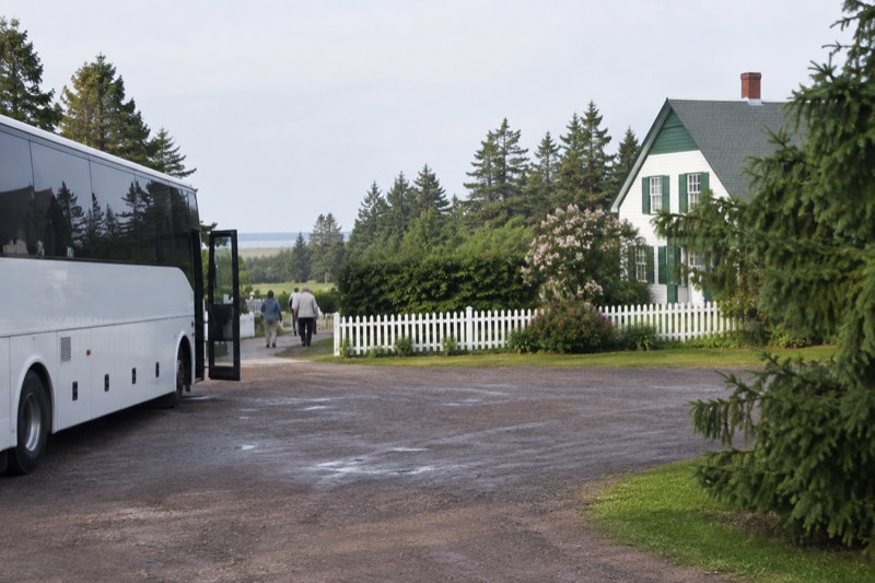 A tour coach parked beside Green Gables House and its green garden hedges