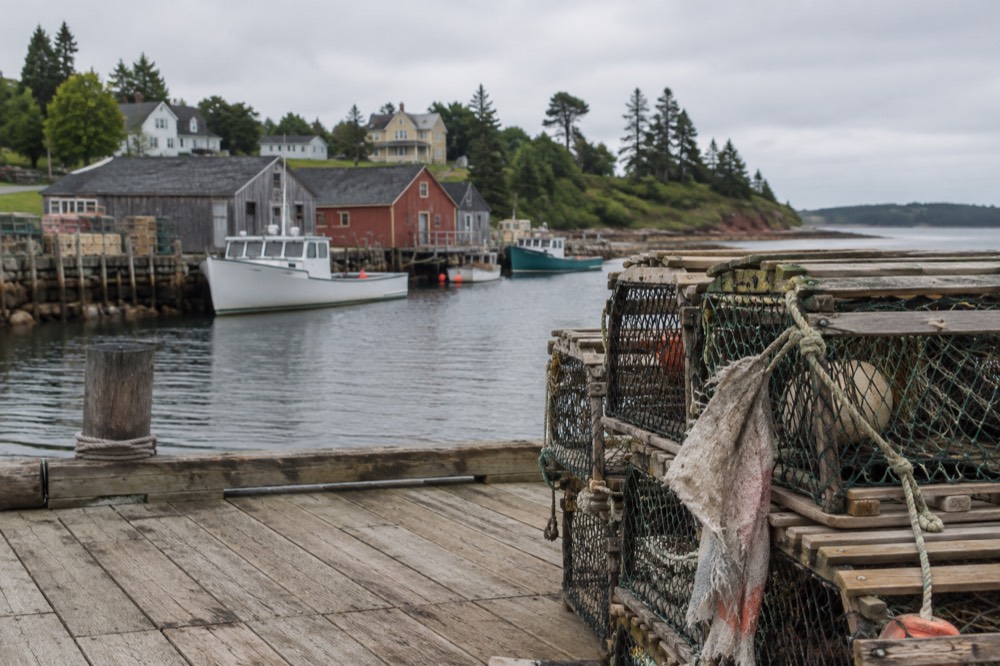 Lobster traps stacked on a wharf with fishing boats in the background