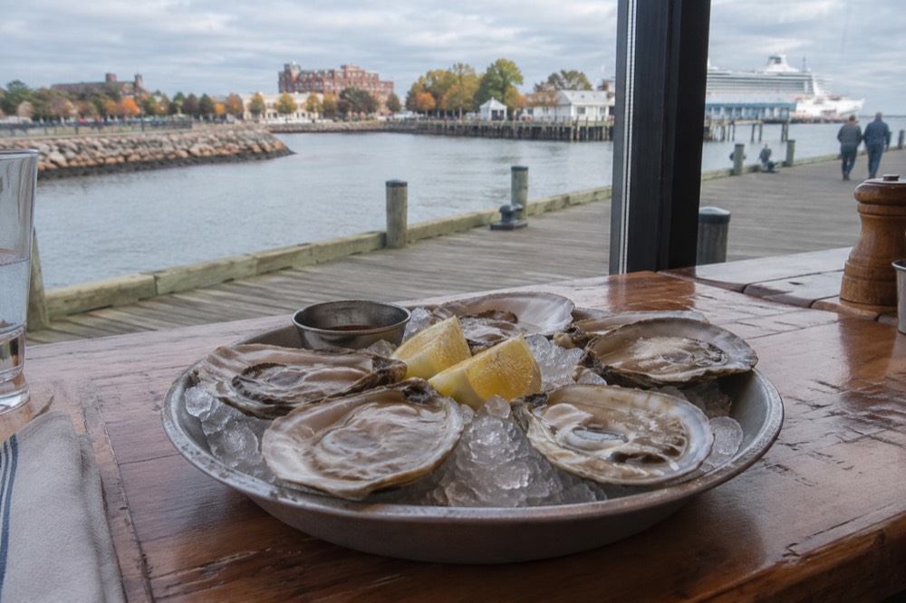 A plate of fresh shucked oysters on ice beside lemon wedges