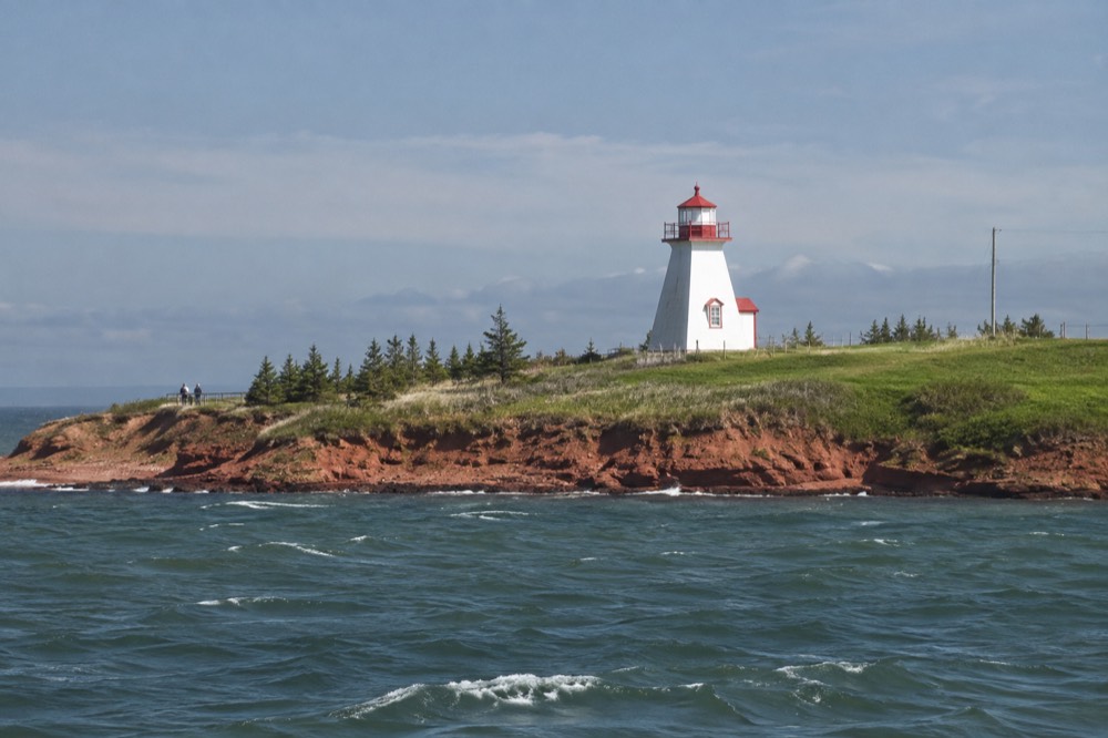 A red lighthouse on a green headland overlooking the sea