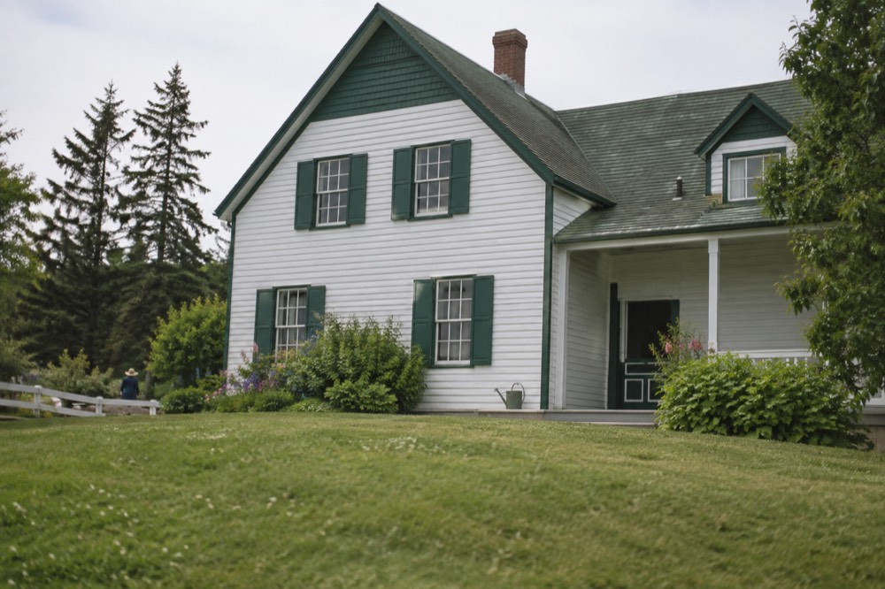 White farmhouse with green gables surrounded by trees and gardens