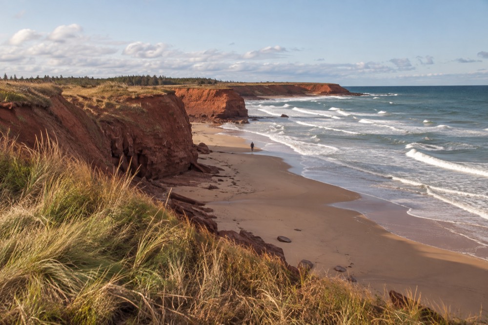 Red cliffs dropping to a sandy beach with rolling waves below