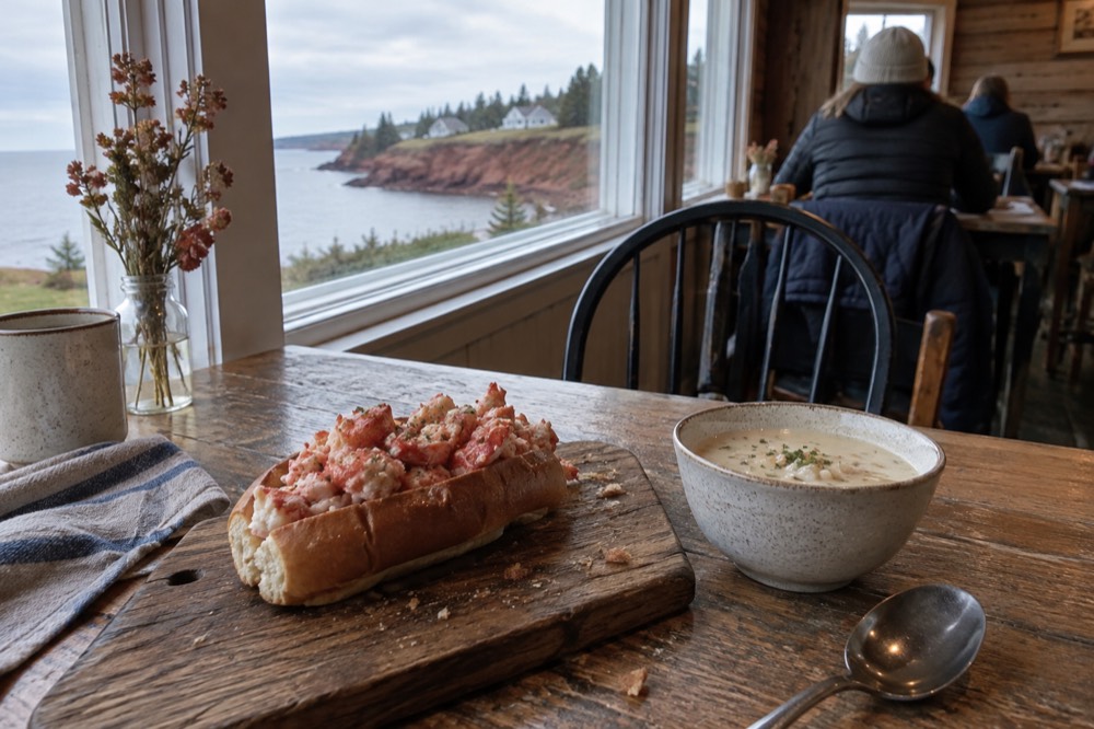 Fresh lobster roll served on a wooden board beside a bowl of chowder