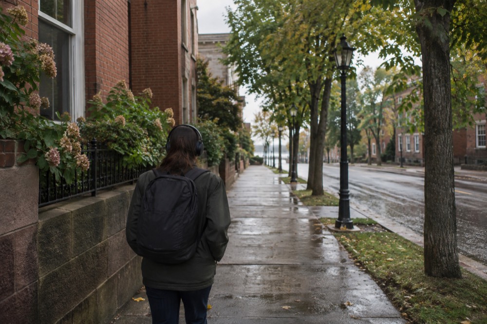 Visitor walking alone past heritage storefronts with headphones in place