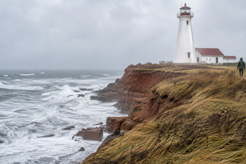 A white lighthouse standing on a red cliff above the sea