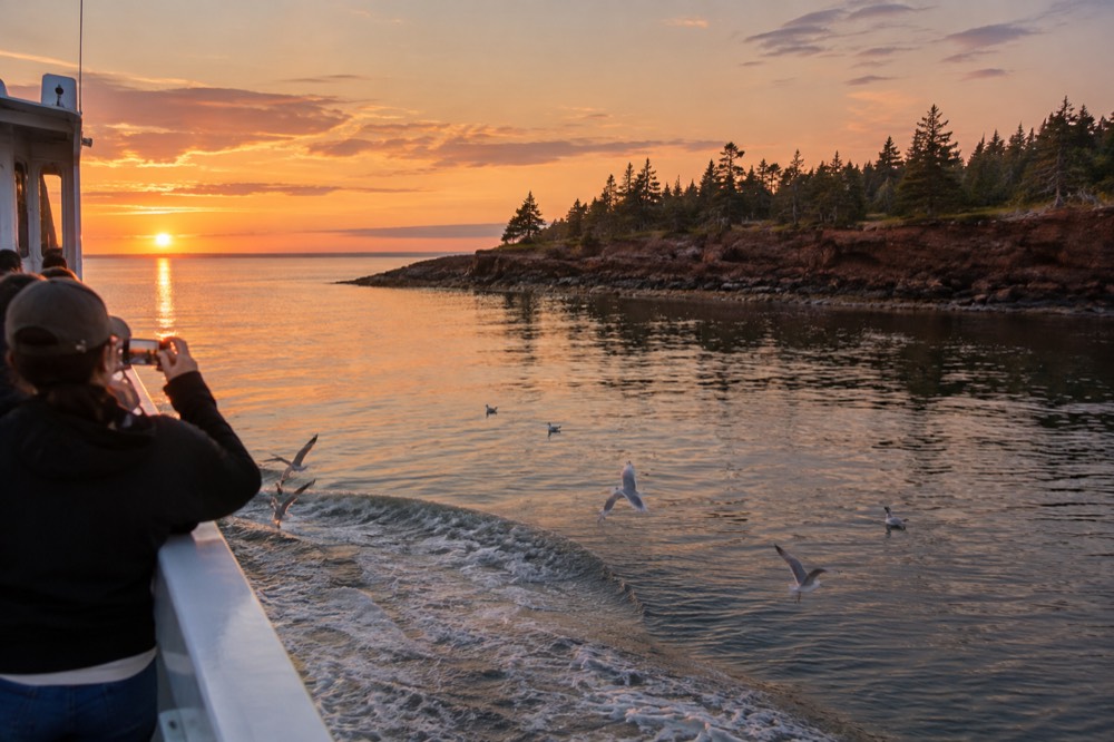 A small tour boat cruising past a rocky shoreline at sunset