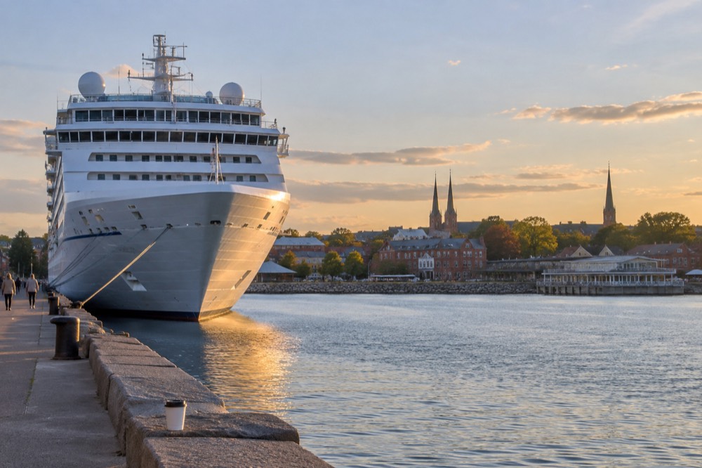 A cruise ship tied up at a waterfront wharf beside a small city skyline