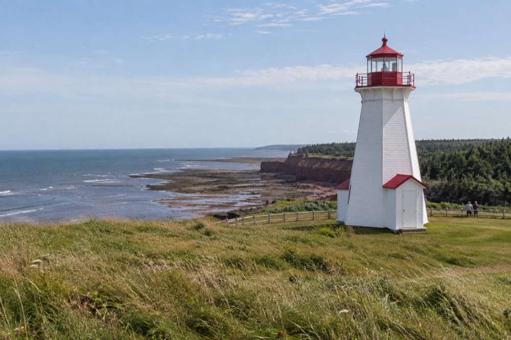 A white lighthouse above a grassy headland overlooking the sea