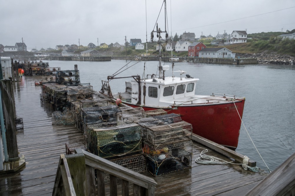 Lobster traps stacked on a wooden wharf beside a red fishing boat