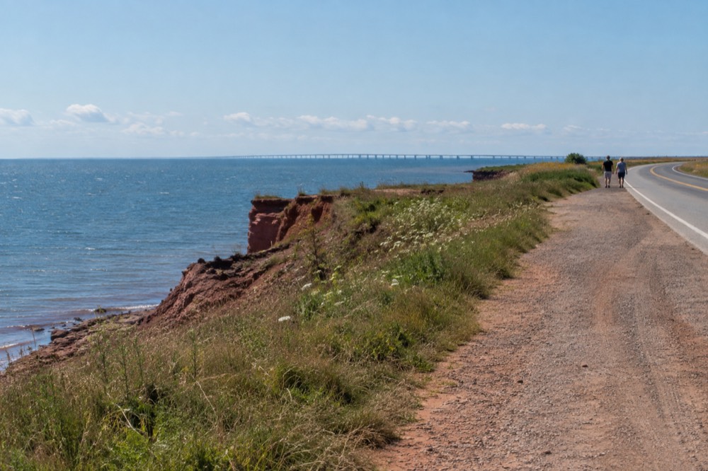 A coastal road with red cliffs on one side and a calm blue sea on the other