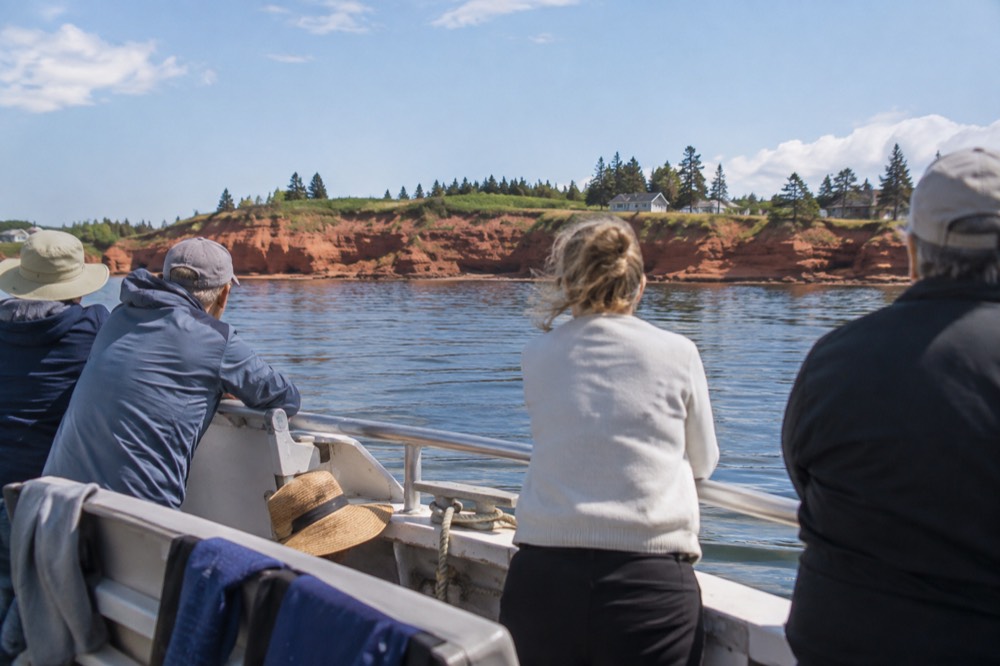 Tour boat passengers at railings with red cliffs and calm water behind
