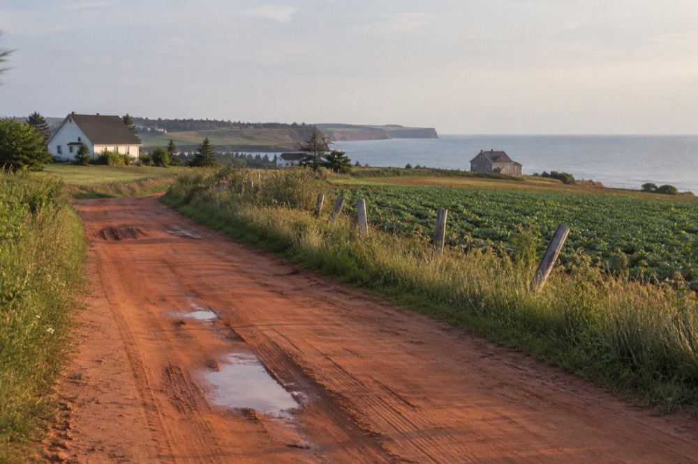 A country road curving past green farm fields toward the sea