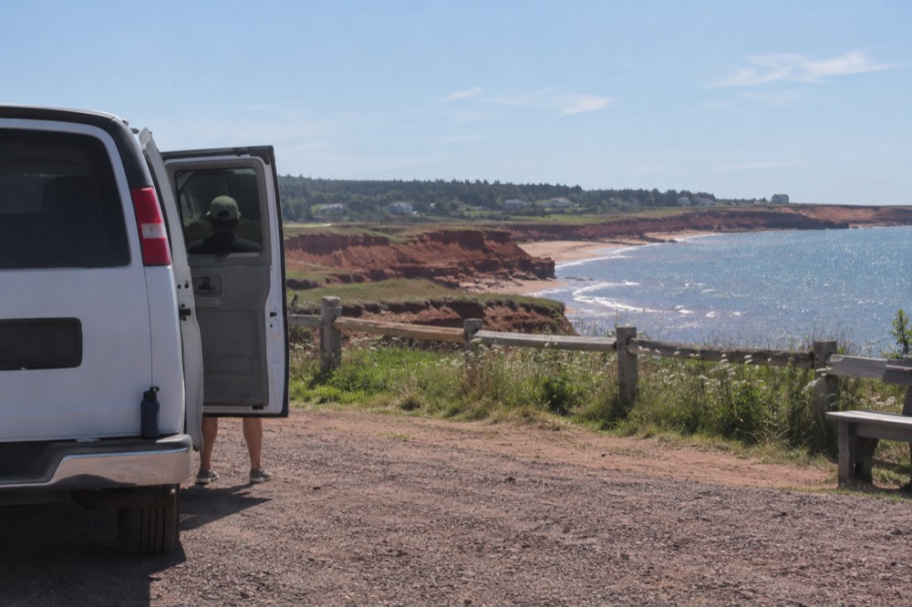 A small tour van parked at a red cliff overlook above the water