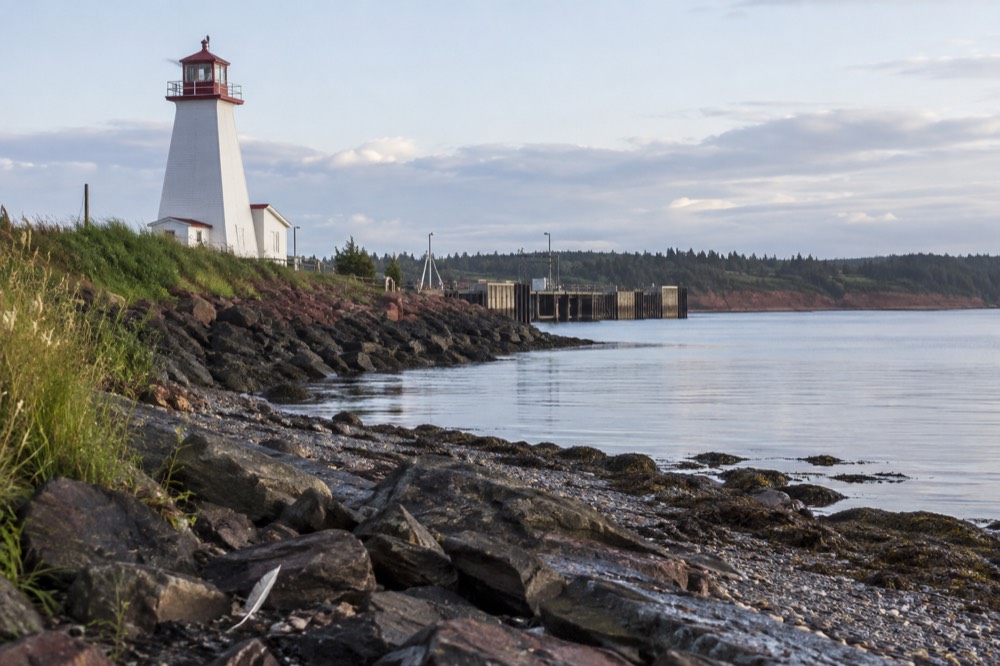 A white lighthouse standing above a rocky shoreline with calm water