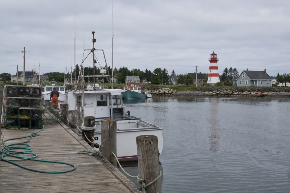 A red and white striped lighthouse above a quiet harbour with fishing boats