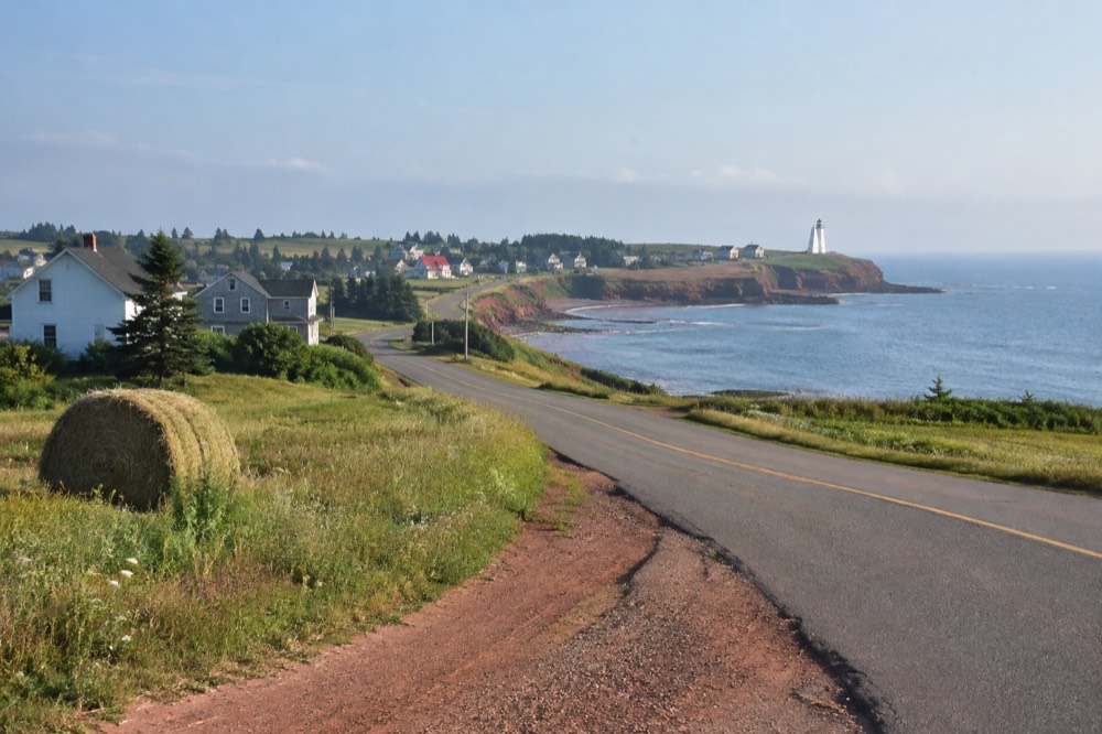 A winding coastal road with a lighthouse visible in the distance