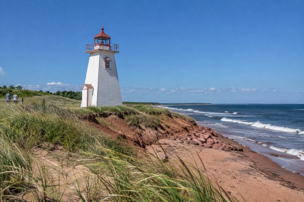 A lighthouse at the end of a red sandstone point under a blue sky