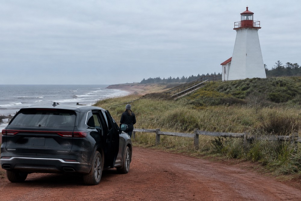 A luxury SUV parked on a coastal road beside a lighthouse