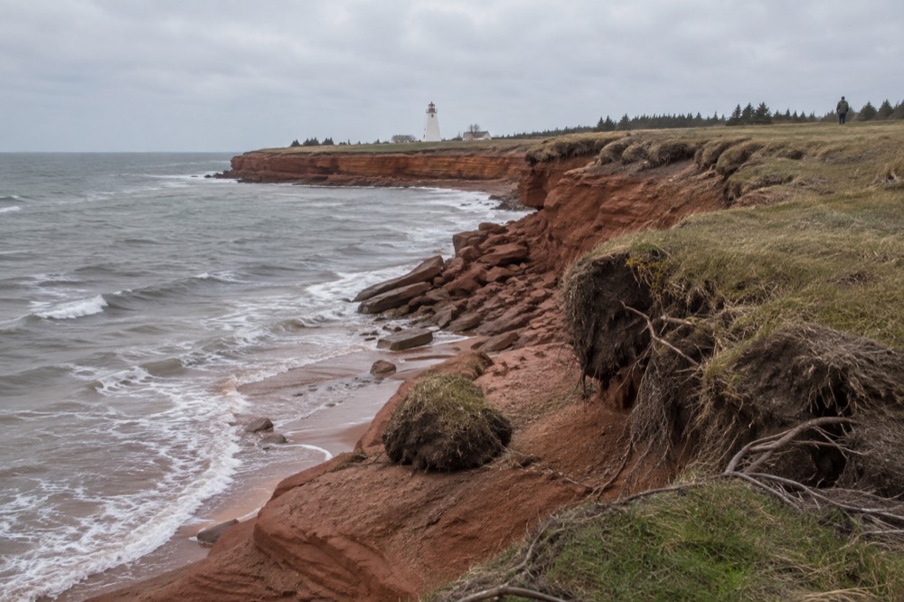 Red sandstone cliffs below a grassy headland with a lighthouse in the distance