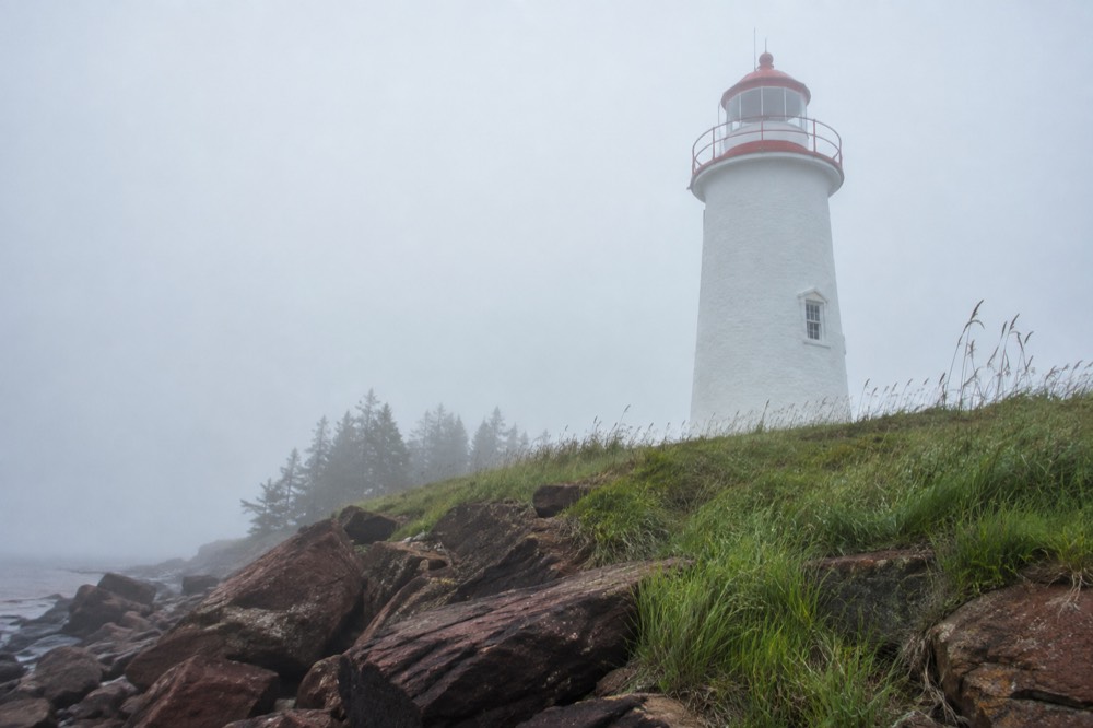 A white lighthouse with a red stripe standing above a rocky point