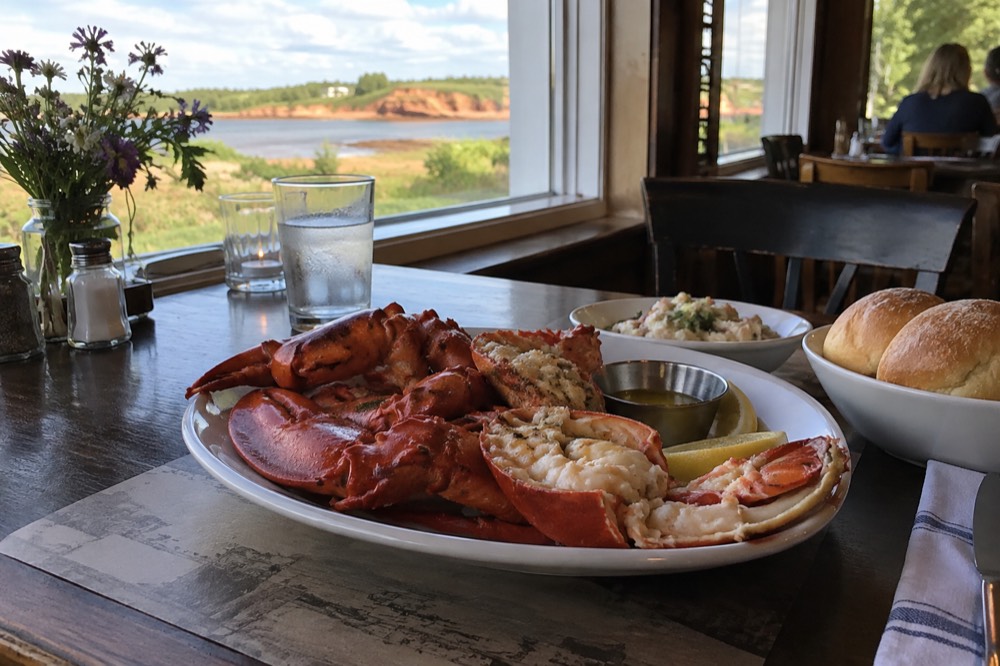 A dining table set with fresh lobster and rolls at a seaside restaurant