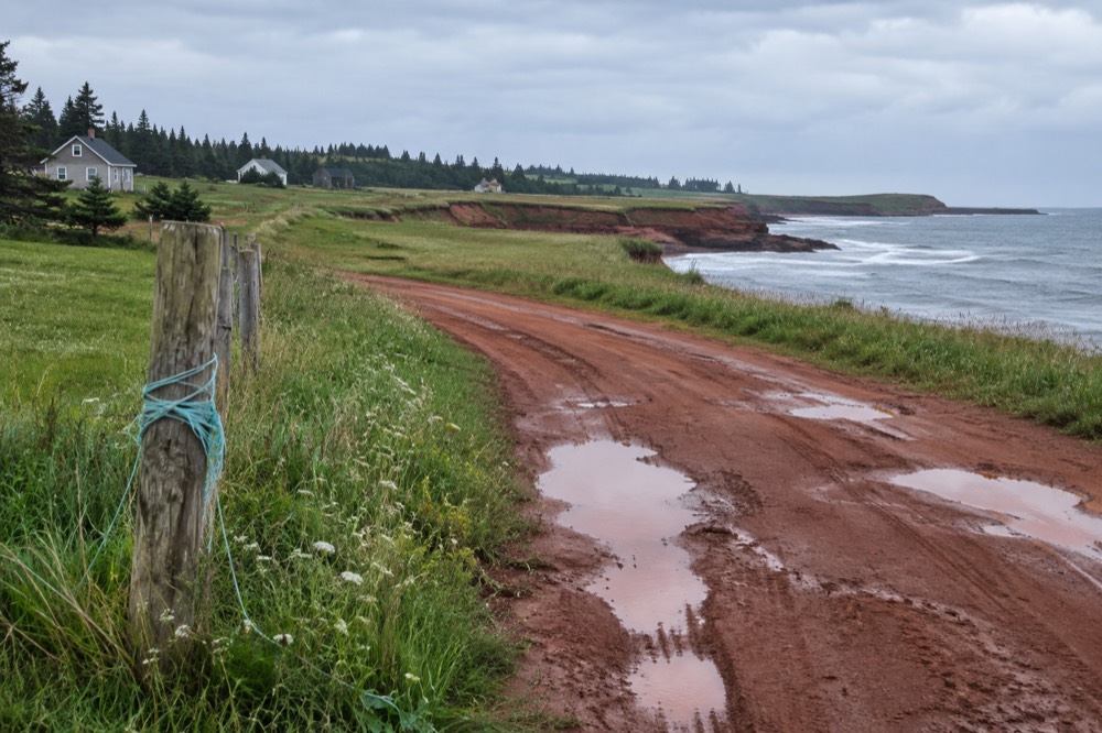 A quiet country road curving past green fields toward red cliffs