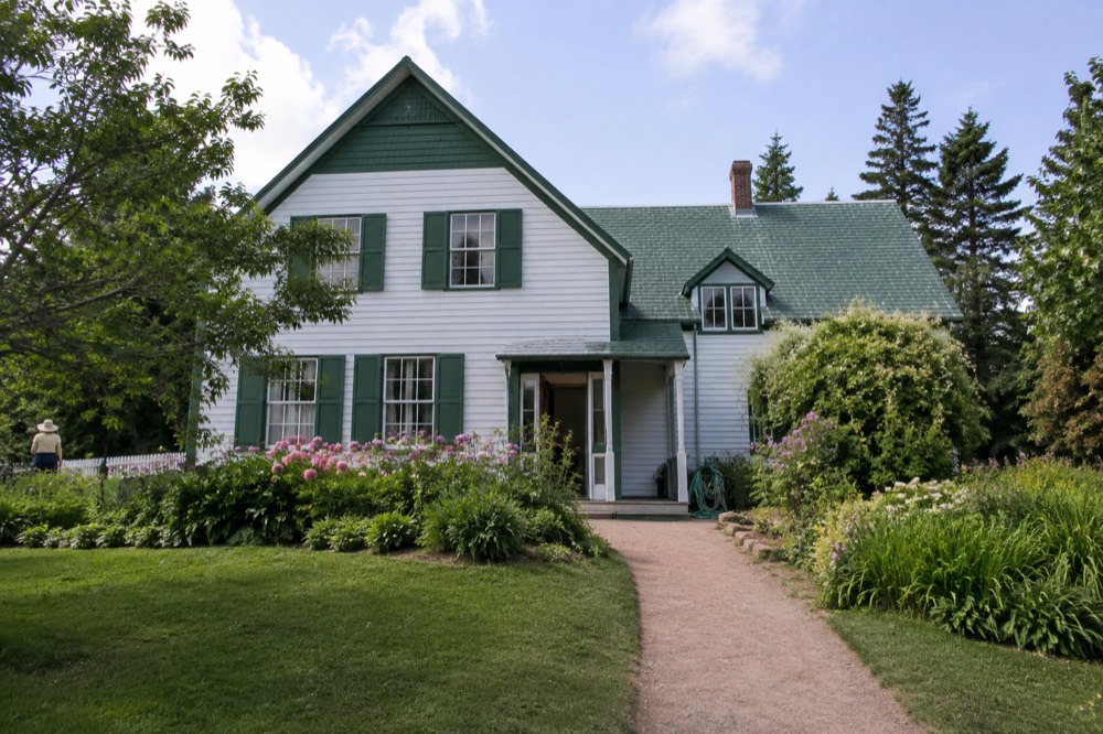 A white farmhouse with green gables surrounded by gardens and trees