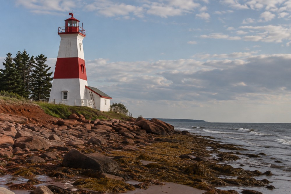 A red lighthouse standing above a rocky shoreline under a wide sky