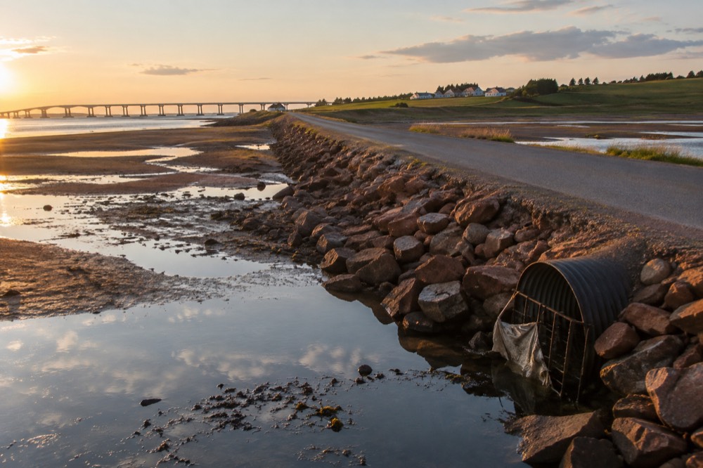 A causeway road crossing red mudflats toward green farmland
