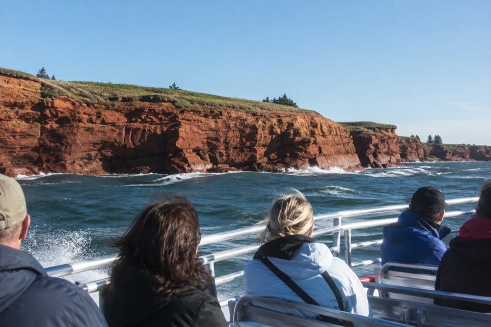 A small boat cruising past a red cliff shoreline