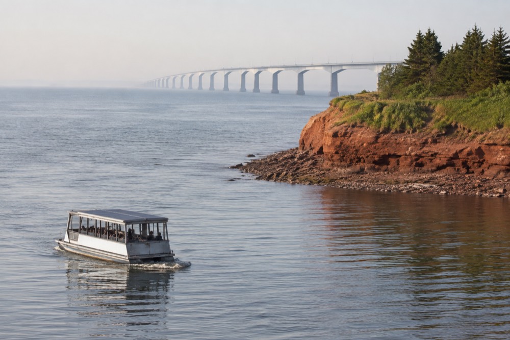 A small solar boat moving slowly past a rocky shoreline with lighthouse